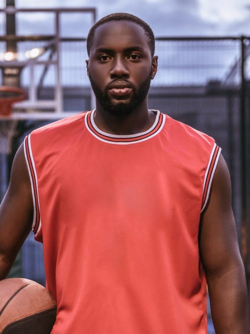 A Black man with a red shirt on a basketball ground holding a basketball.