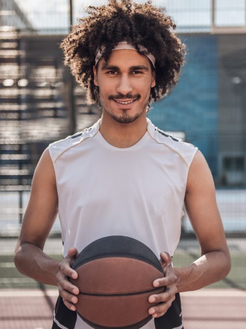 Smiling basketball player holding a ball on an outdoor court
