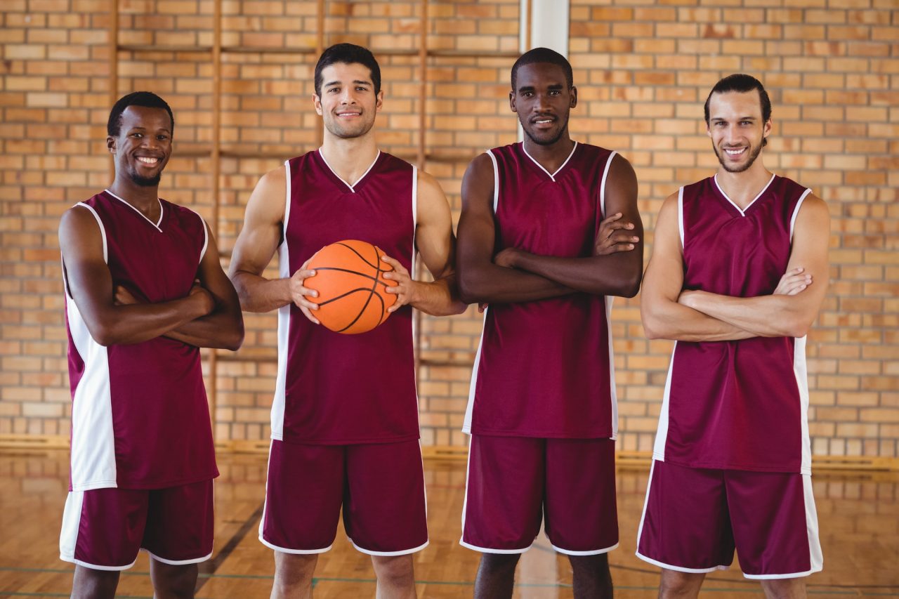 Four confident basketball players holding a basketball on the court.