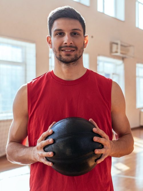 A Red shirt man posing and holding a black ball in hands
